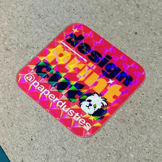 Red rounded-square sticker with a holo square laminate, showing a sparkling prism pattern over the artwork.