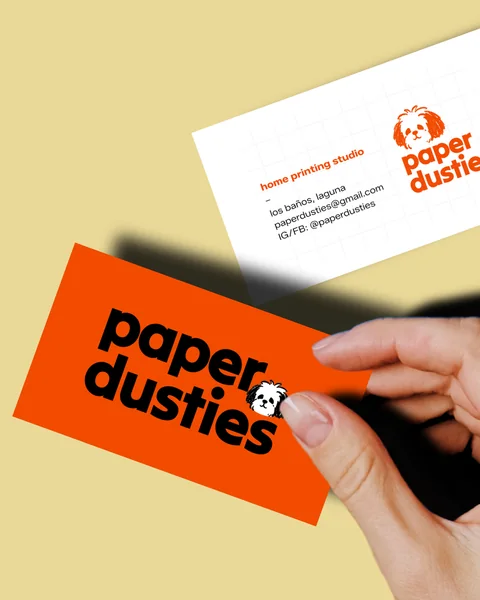 Hand holding an orange Paper Dusties business card beside a white card with the logo.