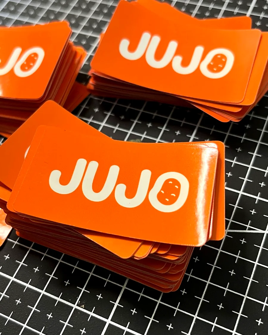 Stacks of orange rounded-corner stickers with a white logo, on a cutting mat