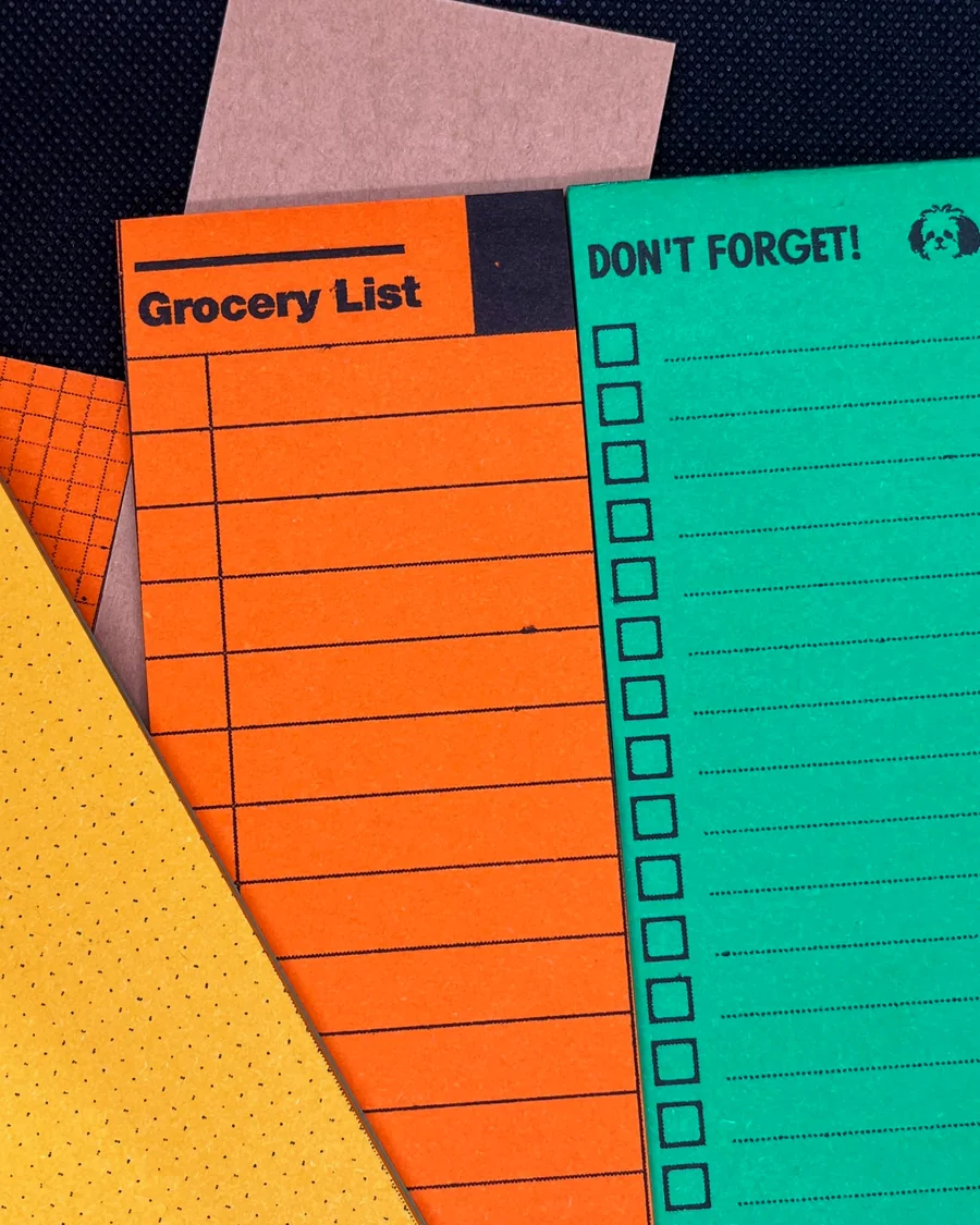 Orange grocery list and green checklist RISO notepads on dark fabric