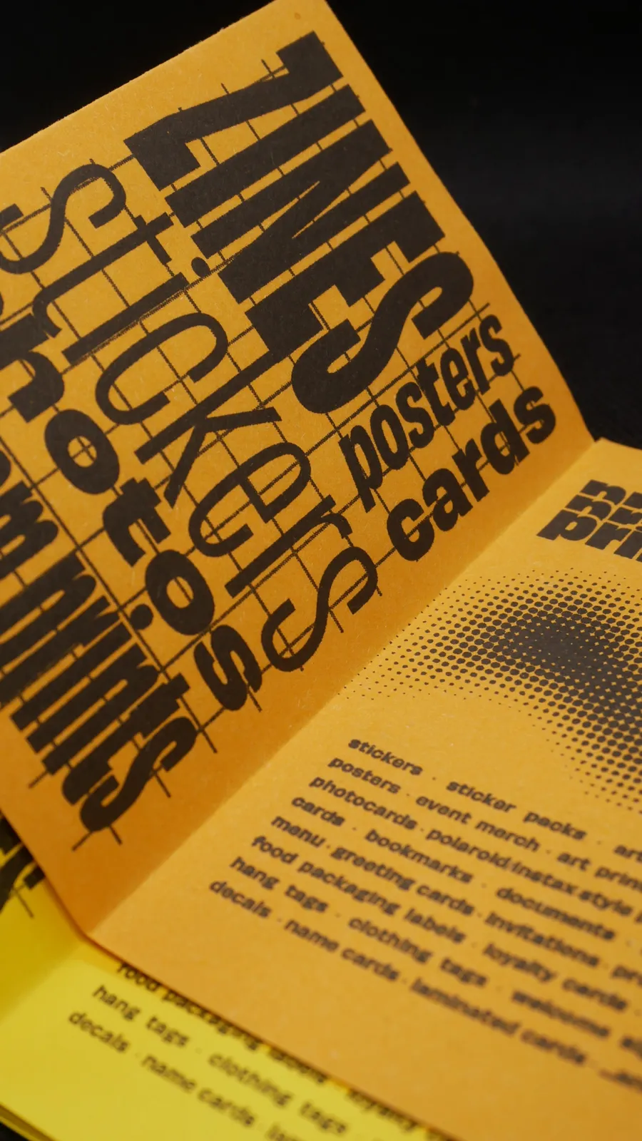 Open RISO zine spread on orange paper with bold lettering that lists zines, stickers, photos, posters, and cards