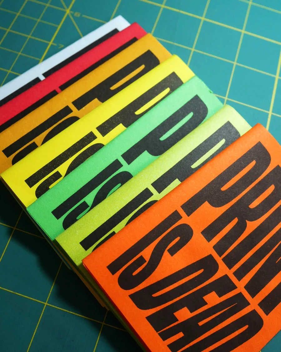 Stack of RISO-printed zines with bold black lettering on bright colored paper